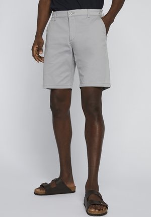 Pantaloncini grigio chiaro in cotone, con taglio classico, fronte piatto e due tasche laterali; indossati con sandali marrone scuro.