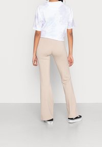 Cropped witte tie-dye t-shirt gecombineerd met beige flared pants en zwarte platform sneakers, met een focus op soepele stoffen en een ontspannen pasvorm.