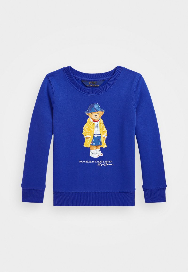 Mėlyna medvilninė palaidinė su ilgomis rankovėmis, su braižu, kuriame pavaizduota meška geltonais rūbais ir mėlyna kepure, baltais batais.