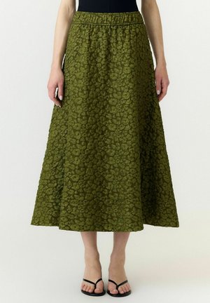 Jupe midi verte texturée avec taille élastique, portée avec un haut noir et des sandales tongs noires, montrée de la taille aux pieds.