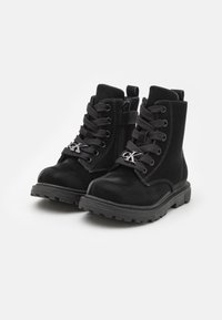 Czarne botki za kostkę wykonane z zamszu o gładkiej fakturze, z okrągłymi noskami, czarnymi sznurówkami, bocznym zamkiem błyskawicznym oraz srebrnym akcentem z logo z przodu.