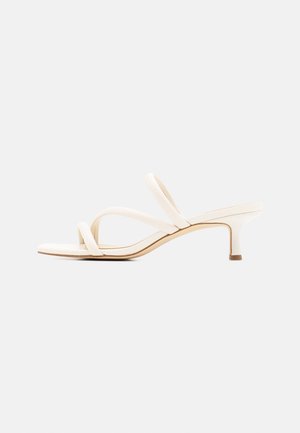 Sandales blanches à talons avec deux brides croisées. Elles présentent un talon bas et cylindrique ainsi qu'une surface lisse et mate au design minimaliste.