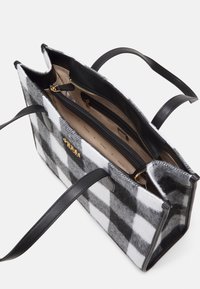 Sac fourre-tout en feutre à carreaux gris et blancs avec des poignées en cuir noir, doté d'une poche intérieure zippée et d'un accent logo doré.