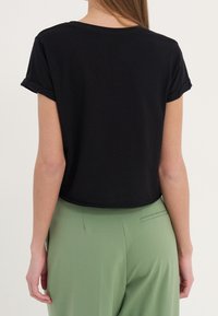 Zwarte cropped t-shirt met opgerolde korte mouwen, gemaakt van ribstof, gecombineerd met lichtgroene hoog-getailleerde broeken.