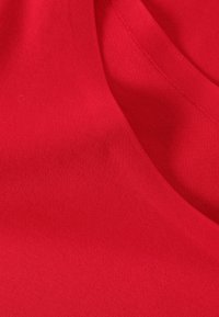 Teflon roșu din bumbac cu o textură fină, având un guler în formă de V și un luciu subtil. Materialul se pliază ușor, arătând detalii de cusătură.