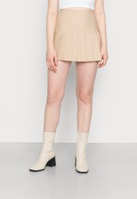 Beige rutigt minikjol med veckad fåll, tillverkad av lättviktig tyg. Bärs med krämfärgade ankelskor med blockklack.