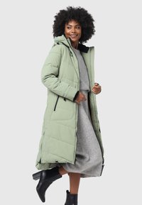 Long, light green puffer coat with a hood, featuring quilted texture, zippered side pockets, and a relaxed fit, paired with a gray sweater dress.