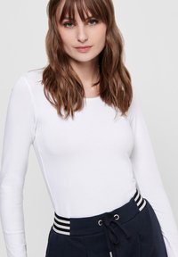 Weißes Langarmoberteil mit glatter Textur, kombiniert mit marineblauen Sweatpants, die einen gestreiften Bund und eine Kordelzugdetail aufweisen.