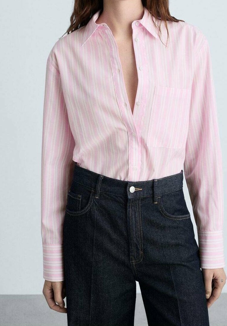 Femme portant une chemise à rayures verticales rose clair rentrée dans un jean bleu foncé taille haute.