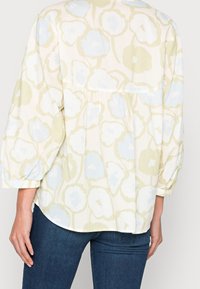 Personne portant un blouse ample à manches longues avec des motifs floraux bleu pâle et beige, associé à un jean ajusté bleu foncé, vue de derrière.