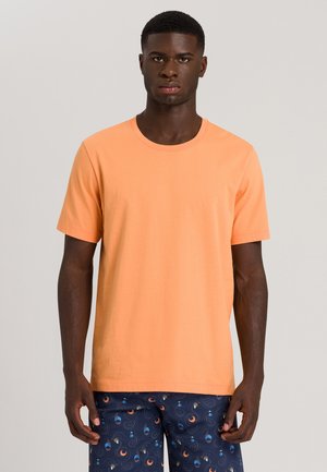 Short-sleeve t-shirt in pastel orange cotton, featuring a round neckline. Worn with patterned navy shorts displaying circular designs.