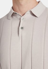 Jasbeżowa koszulka polo o teksturowanym wzorze, z klasycznym kołnierzykiem i dwoma szarymi guzikami przy dekolcie.