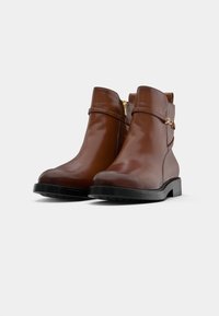 Brown leather ankle boots with a glossy finish, zipper closure, wide strap with gold hardware, and black rubber soles.