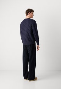 Granatowy sweter dzianinowy z teksturowanym wzorem, okrągłym dekoltem i ściągaczami. W połączeniu z szerokimi czarnymi spodniami i beżowymi butami.
