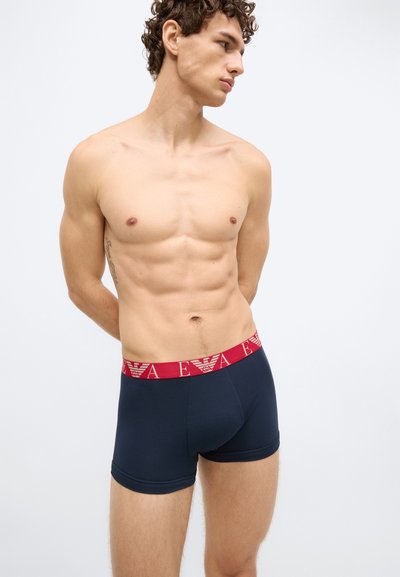 Cuecas boxer azul-marinho feitas de tecido elástico, com cós vermelho decorado com um padrão de logótipos. Pernas ajustadas, com textura suave.