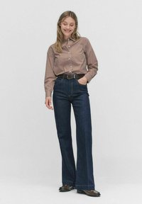 Chemise rayée à boutons marron et crème, associée à un jean bleu foncé évasé. Comprend une ceinture et des chaussures plates au design texturé.