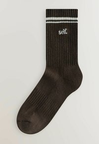 Pruunid ribaga sokid, mille ülaservas on kaks valget triipu, ja külje peal on valge tikandiga sõna "self."