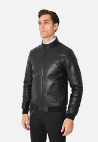 Giacca bomber in pelle nera con chiusura a zip, polsini e orlo a coste, caratterizzata da due tasche anteriori con zip e una texture liscia e elegante.