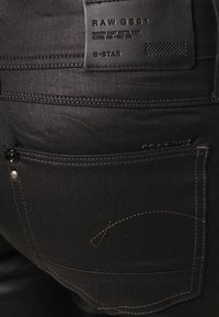 Svarta denimjeans med en läderetikett med varumärke, subtila sömnadsdetaljer och en bakficka med knappstängning.