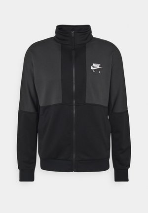 Czarna i ciemnoszara kurtka Nike Air na zamek błyskawiczny z wysokim kołnierzem i białym logo na lewej piersi, długie rękawy oraz ściągacze na mankietach i u dołu.