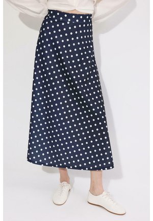 Tumesinine A-lõikeline midi seelik valgete täppidega, kantud valge lühikese toppi ja valgete vabaaja paeltega kingadega.