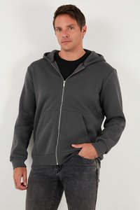 Grå zip-up huvtröja gjord av mjukt material, med en framficka, justerbar huva och ribbade ärmar. Bärs över en svart skjorta.