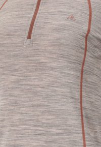 Vaalea harmaa neulepusero, jossa on teksturoitu neulekuvio. Ominaisuuksina on puolivetoketju kaula-aukossa ja kontrastiväriset ruosteenväriset ompeleet. Pieni logo rinnassa.