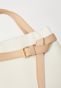 White leather handbag with beige straps, featuring a gold buckle detail, and textured surface. Minimalist design and clean lines.