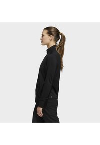 Schwarzes sportliches Sweatshirt mit hohem Kragen und strukturiertem Stoff. Hat ein eng anliegendes Design und gerippte Bündchen, präsentiert in einer Seitenansicht.