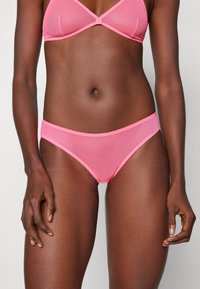 Slip bikini seamless rosa con una texture liscia e un design minimalista. Presenta un cinturino elastico e un bordo in pizzo floreale abbinato.