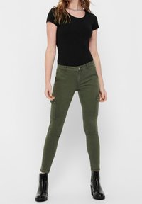 Olivgröna cargobyxor tillverkade av bomullsblandning, med fyra fickor, slim-fit design och knappstängning, kombinerade med en svart topp.