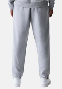 Hellgraue Jogginghose aus weichem Stoff, mit elastischem Bund und seitlichen Taschen, kombiniert mit weißen Turnschuhen.