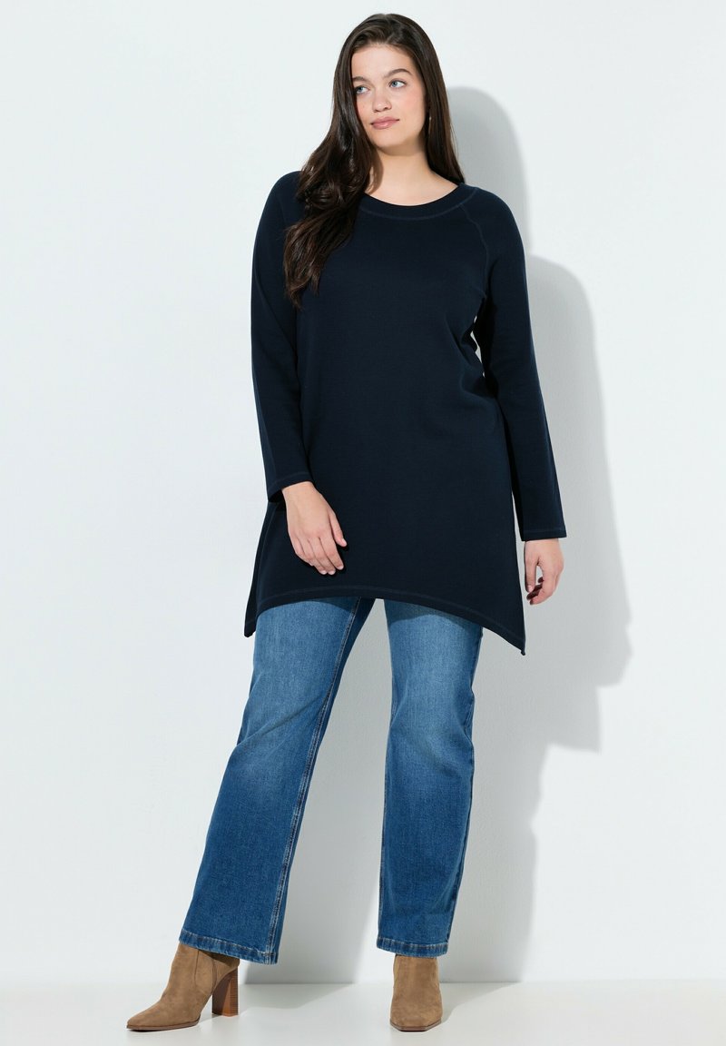 Marineblauwe tuniek met lange mouwen, een ronde halslijn, een asymmetrische zoom en een gestructureerde stof, gecombineerd met lichtblauwe denim en beige enkellaarsjes.