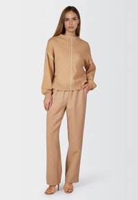 Beige knit sweater with a crew neck, featuring white stitching details and ribbed cuffs, paired with light beige wide-leg trousers.