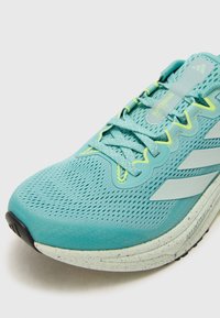 Zapatilla de running azul claro con parte superior de malla transpirable, detalles en amarillo, rayas grises y una mediasuela moteada. Los cordones son planos y texturizados.