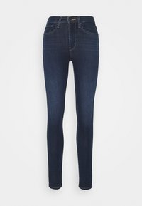 Jeans ajustados de color azul oscuro con bolsillos frontales, trabillas para cinturón y cierre de botón sobre un fondo blanco plano.