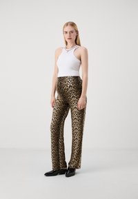 Bela rebrasta majica na bretele u kombinaciji z leopard uzorkom zakrčenih hlača, koje imaju sjajnu teksturu i neutralnu paletu boja. Crne cipele upotpunjuju izgled.
