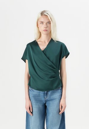 Green draped blouse in a smooth fabric, featuring a V-neck and short sleeves, paired with light blue wide-leg jeans.