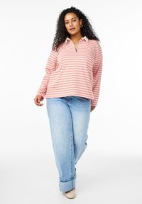 Pullover a righe in rosa pallido e crema con colletto a mezza zip. Abbinato a jeans azzurri a gamba larga e scarpe beige. Tessuto morbido.