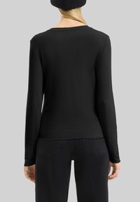 Zwarte langemouwen shirt van zacht materiaal, met een ronde hals en geschulpte zoom. Draagt met donkere broeken.