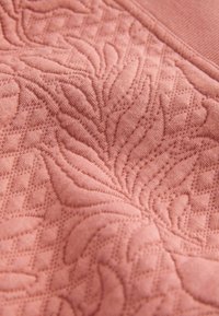 Prim-plan al unui material roz cu modele florale și de diamant umflate, creând designuri texturate de frunze și geometrice.