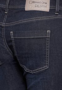 Ciemnoniebieskie dżinsy z prostym wzorem kieszeni z tyłu, jasnym przeszyciem i prostokątną metką marki w pobliżu pasa.