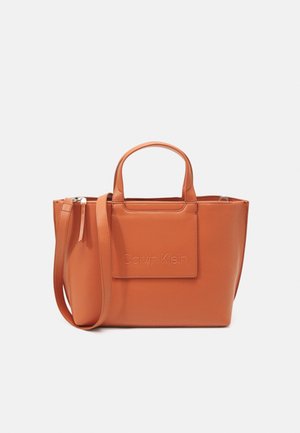 Calvin Klein oranssi nahkainen olkalaukku, muotoiltu malli, ylhäältä suljettava vetoketju, lyhyet kahvat, kohokuvioitu logo, säädettävä olkahihna.