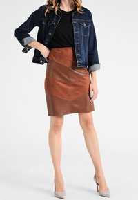 Veste en denim au design classique, associée à une jupe en cuir brun avec des détails en panneaux, et des escarpins gris clair.