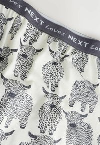 Boxershorts met een grijze tailleband met de tekst "NEXT Loves". Versierd met zwart-wit geïllustreerde vee op een crèmekleurige achtergrond.