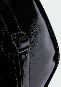 Borsa nera lucida con una superficie testurizzata, dotata di una fibbia in metallo argentato sulla tracolla e di una forma liscia e arrotondata.