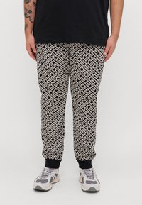 Joggers con un diseño geométrico en negro y crema, con puños elásticos y un ajuste relajado. Combinados con zapatillas grises y blancas.