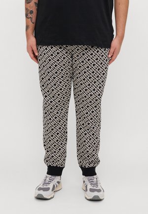 Pantalons de jogging noirs et crème avec un design géométrique, des poignets élastiques et une coupe décontractée. Associés à des baskets grises et blanches.