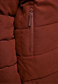 Doudoune de couleur bordeaux riche avec une texture lisse et douce. Comprend une poche latérale zippée avec un détail de fermeture éclair assortie.