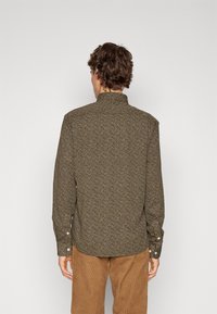 Camicia marrone a fantasia con colletto, maniche lunghe e polsini con bottone. Presenta un tessuto texturizzato con un mix di colori nel motivo.